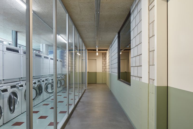 Lise & Lotte, Umbau und Umnutzung Sägestrasse 76/78, Köniz – Gemeinsame Waschküche im Norden mit Glaswand zum Korridor, auf dem Niveau vom Hofgeschoss – Edward Greiner
