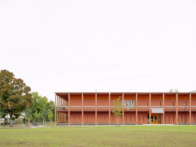 AVS Amt für Verbraucherschutz Kanton Aargau – Ein rötlicher Farbauftrag fasst die Aussenbauteile zusammen und schützt das Holz vor Witterung. Aus der Ferne wirkt das Gebäude wie eine rötliche Wolke. Doch je näher man tritt, desto bunter und differenzierter zeigt sich der Farbaufbau. Bild: Ansicht Südost – Federico Farinatti